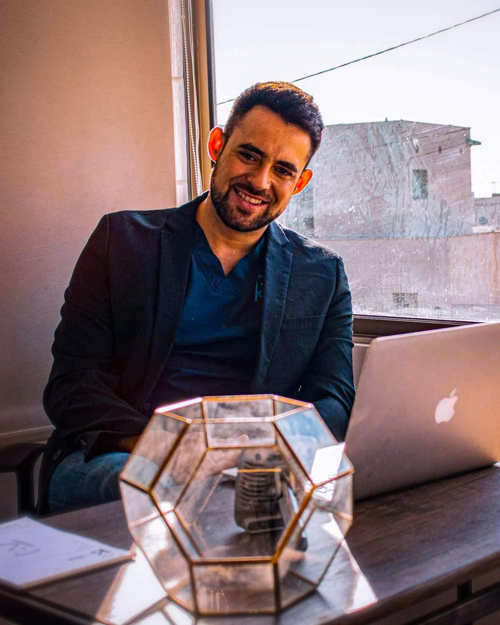 Adolfo Villalón Sandoval sonriendo, sentado en su escritorio junto a una ventana